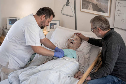 Person mit Pflegegrad 5 erhält intensive häusliche Pflege durch eine Pflegekraft und Unterstützung durch Angehörige.